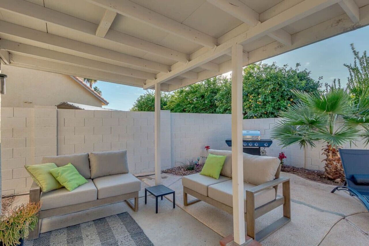 An outdoor patio with a covered seating area, a barbecue grill, and a potted plant.