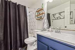 Ein Badezimmer mit einer weißen Toilette, einer Duschvorhang, einem Waschbecken mit Spiegel und einem Handtuch an der Wand.