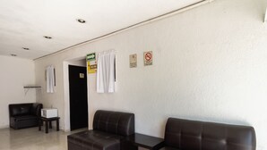 Un vestíbulo de hotel con mostrador de recepción, dos sofás de cuero, una mesita y una puerta que da a otra habitación.