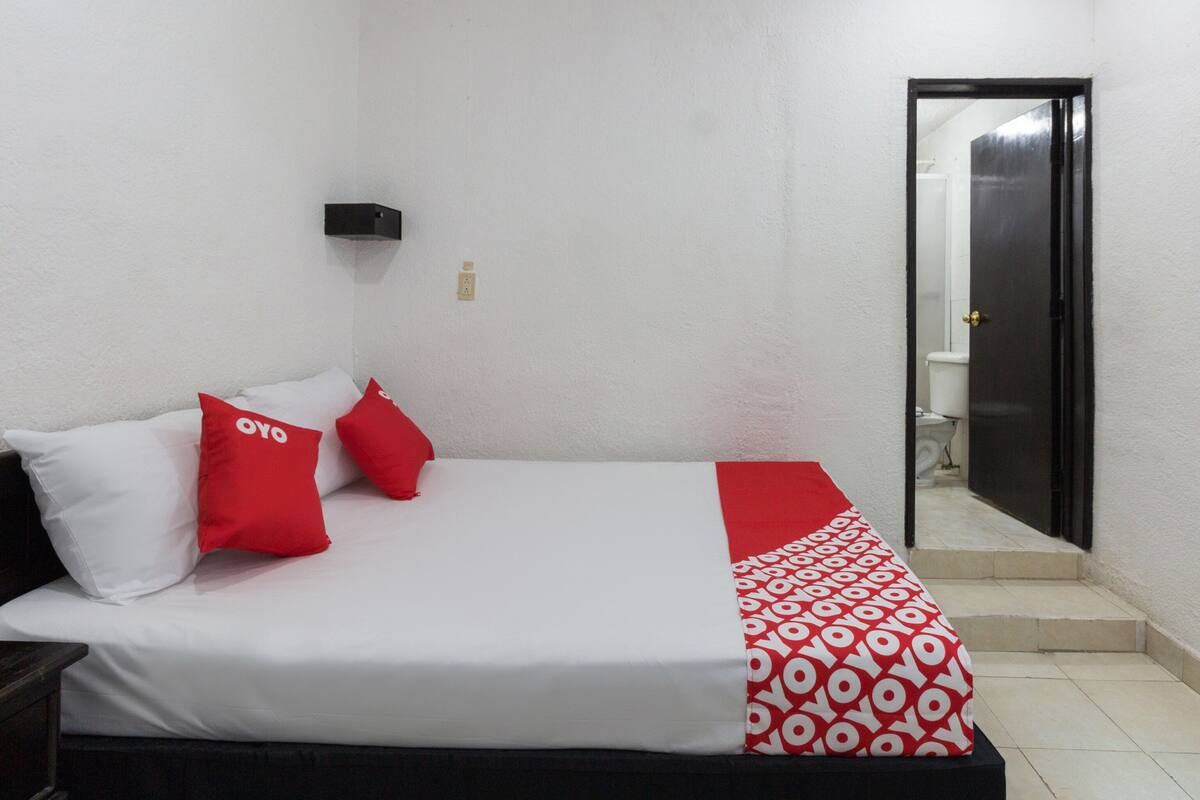 A bedroom with a bed, white walls, a black door, and a red and white patterned blanket.