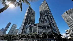 A modern high-rise building with a curved facade, surrounded by palm trees and a clear blue sky.