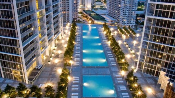 A high-rise hotel with multiple swimming pools, arranged in a central axis, surrounded by tall buildings.