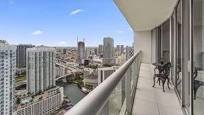 A high-rise building with a balcony overlooking a cityscape, including a river and various buildings.