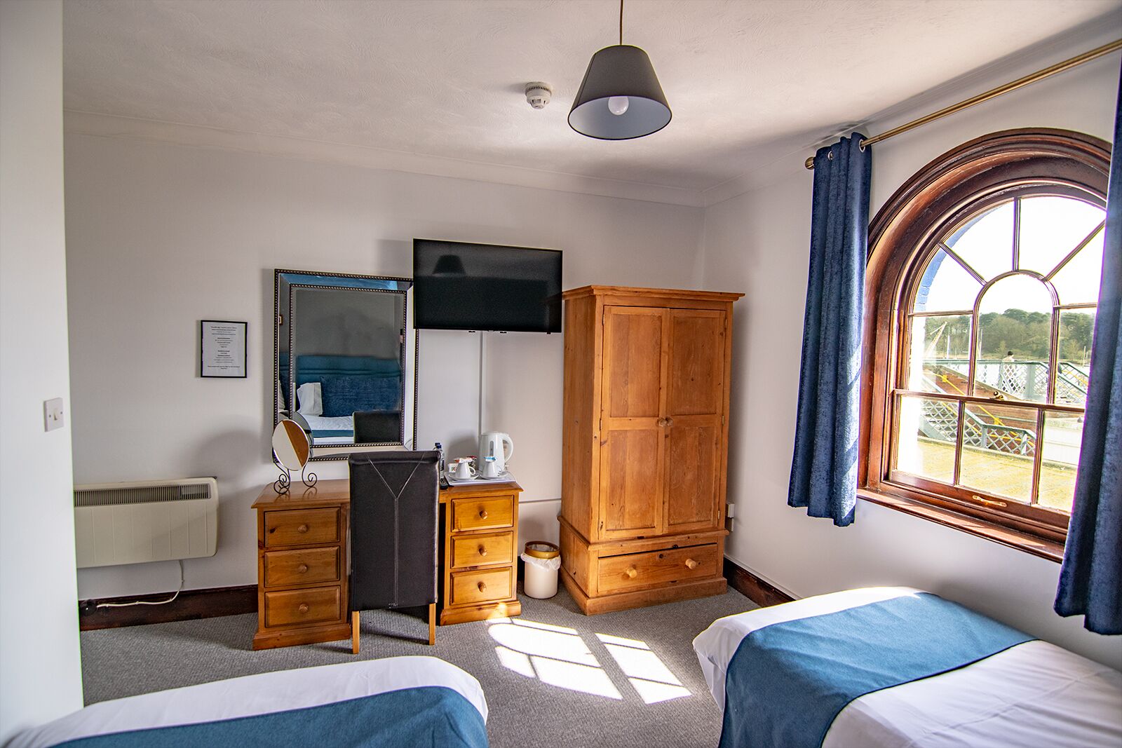 Habitación de hotel con dos camas, un armario, un escritorio con espejo, un televisor y una ventana con cortinas.