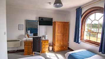 Habitación de hotel con dos camas, un armario, un escritorio con espejo, un televisor y una ventana con cortinas.