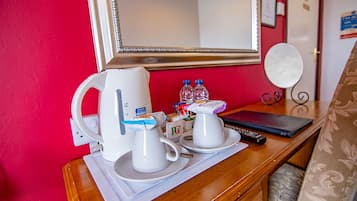 A hotel room with a wooden desk, a white kettle, two white cups, a plate, a remote control, and a mirror.