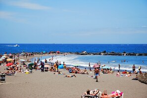Une plage bondée où les gens se prélassent au soleil et se baignent, et un bateau sur l’eau.