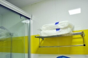 Bathroom features a glass shower enclosure and a yellow-tiled wall, along with a towel rack and two white towels.