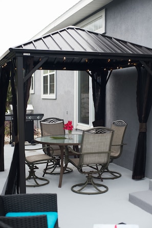 Relax in a serene outdoor setting with a covered patio featuring a round table and four comfortable chairs.
