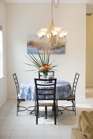 Enjoy meals in this elegant dining area with a round table for four, a vase with fresh flowers, and a chandelier above.