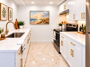A modern kitchen with white cabinets, gold handles, and a marble floor.