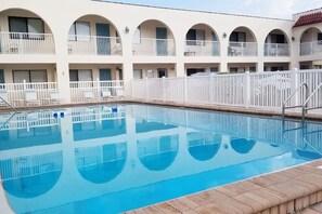 Une piscine entourée d’une clôture blanche, elle-même bordée d’un immeuble doté de nombreux balcons.