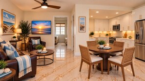 A modern living room with a sofa, coffee table, and dining area with chairs. There is a kitchen with white cabinets and stainless steel appliances.