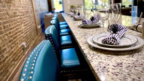Una larga mesa de comedor con sillas tapizadas en azul, dispuesta con platos, vasos y servilletas a rayas.