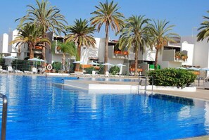 Une piscine bordée de palmiers et entourée de chaises longues, le tout niché au milieu d’immeubles modernes.