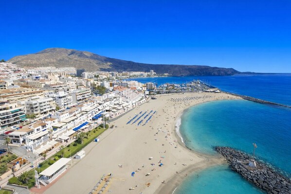 A coastal cityscape with a beach, buildings, and a mountain in the background.