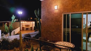 A balcony with a table and chairs, a cactus plant, and a building with a light fixture in the background. - Casitas del Valle  (Valle de Guadalupe)