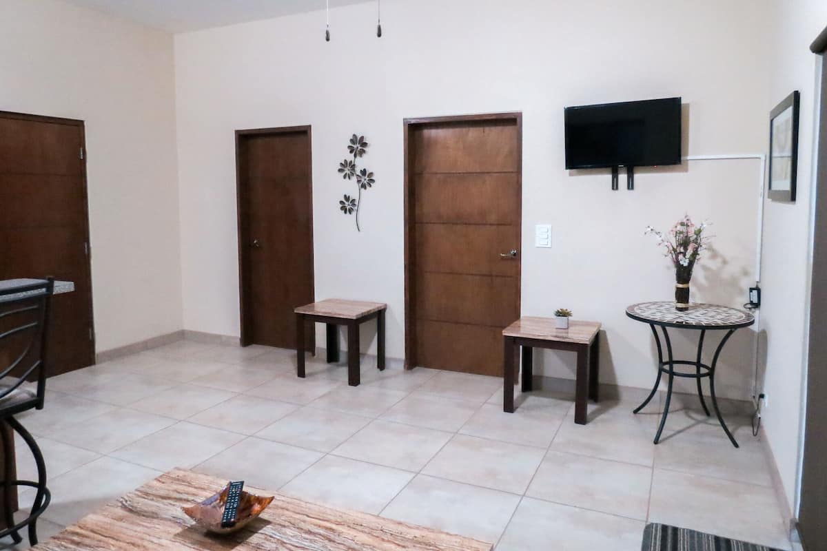 A living room with a TV mounted on the wall, a small table with a vase of flowers, and a chair.