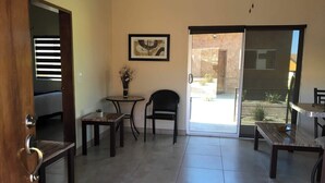 A room with a dining area, a small table with a vase of flowers, a chair, and a sliding glass door leading outside. - Casitas del Valle  (Valle de Guadalupe)