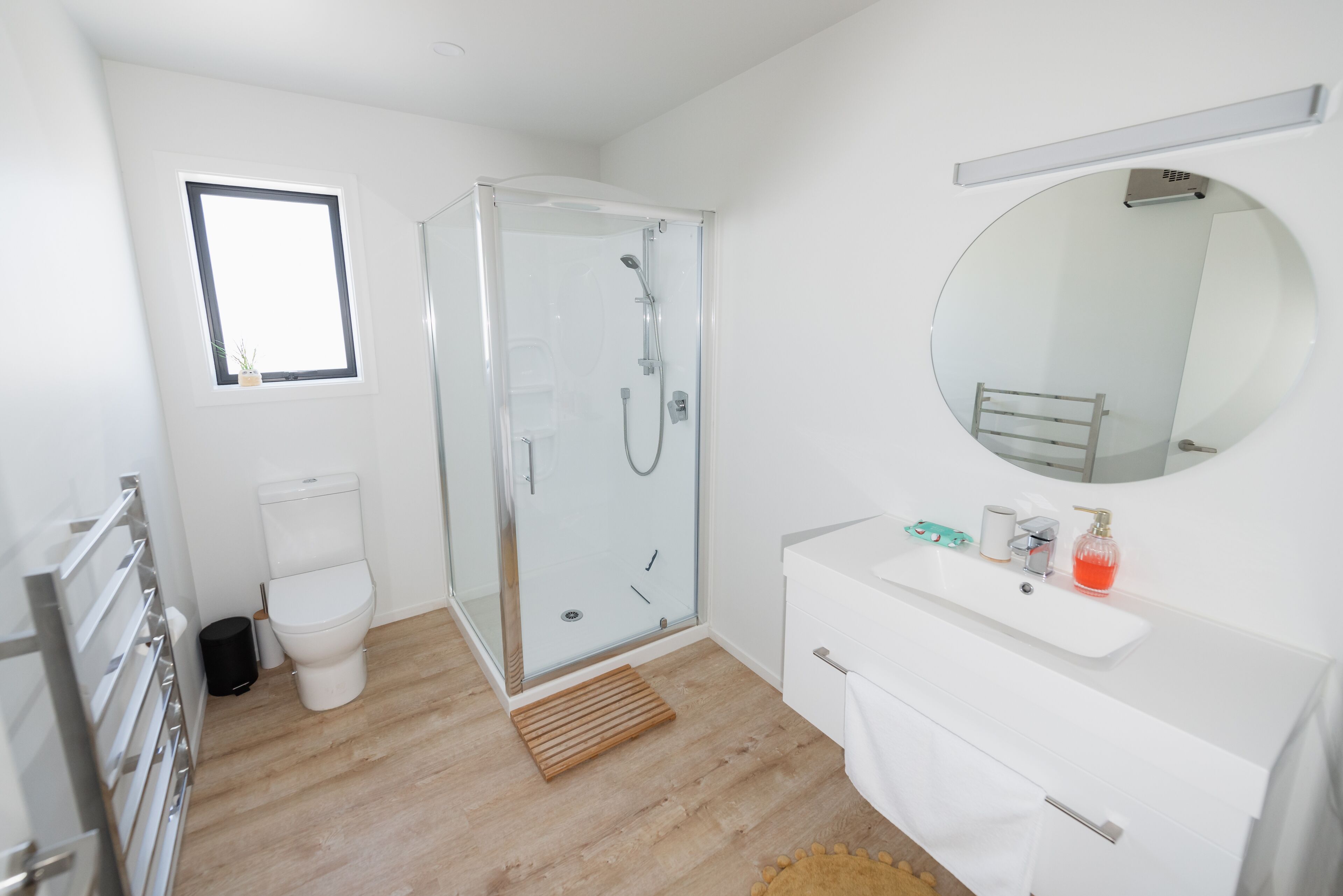 Een moderne badkamer met een douche met glazen wand, een wit toilet, een wastafel met spiegel en een klein raam.