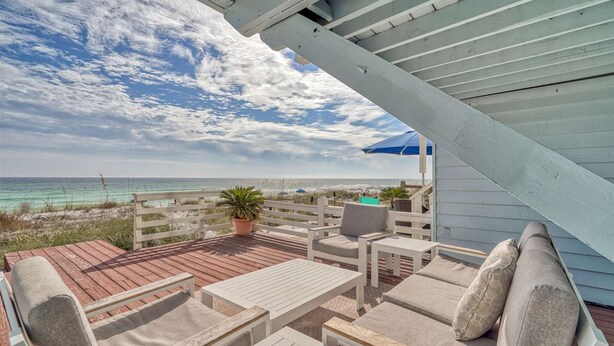 Eine Holzterrasse mit Gartenmöbeln, einem Blumentopf und Blick auf Strand und Meer.