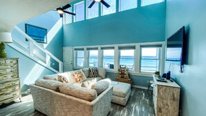 Ein Wohnzimmer mit einem großen Ecksofa, einer Treppe und Blick aufs Meer.