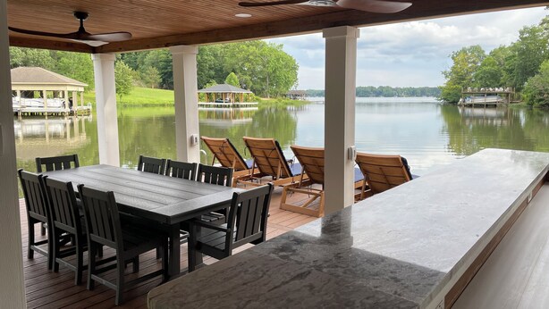 A covered outdoor area with a table and chairs, a view of a lake, and a gazebo in the background.