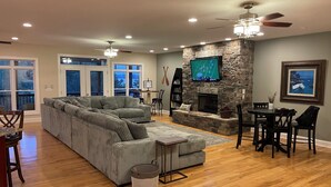 A living room with a stone fireplace, a large sectional sofa, and a dining area with a table and chairs.