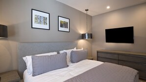 Un dormitorio moderno con una cama grande, una mesita de noche, un televisor montado en la pared y dos cuadros enmarcados.