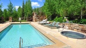 Una piscina rectangular con borde de piedra, rodeada de sillas de descanso y un jacuzzi.