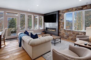 A modern living room with a fireplace, large windows, and a stone accent wall. - Newly remodeled modern condo. Pool/hot tubs. Walk to town over pedestrian bridge (Vail)