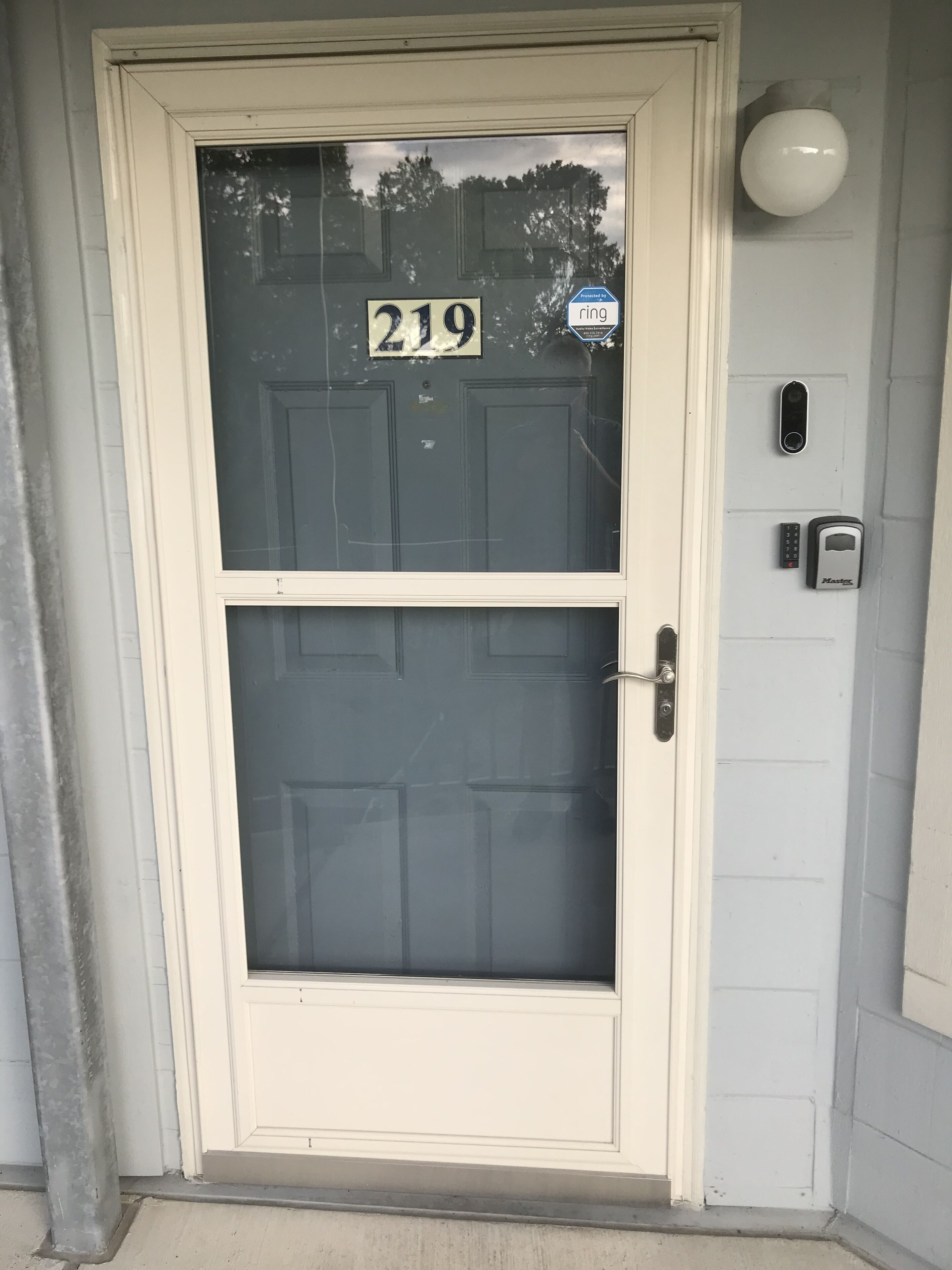 Eine Haustür mit Nummernschild '219', einem Fenster, einer Türklinke und einem an der Wand montierten Gegensprechanlage.