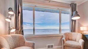 A room with two armchairs, a large window with curtains, and a lamp on a side table. - Luxurious Oceanfront Suite - Sleeps 6 - Second Floor - Pool and Sauna! (Lincoln City)
