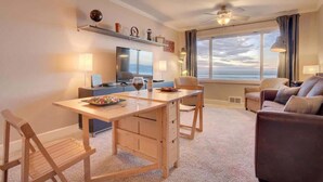 A modern living room with a wooden dining table, a sofa, and a TV. - Luxurious Oceanfront Suite - Sleeps 6 - Second Floor - Pool and Sauna! (Lincoln City)
