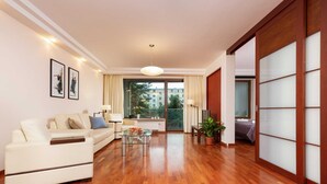 A modern living room with a sofa, a glass coffee table, and a view of the outdoors through large windows. - Modern Apartment in the Center | Balcony | Parking (Warszawa)