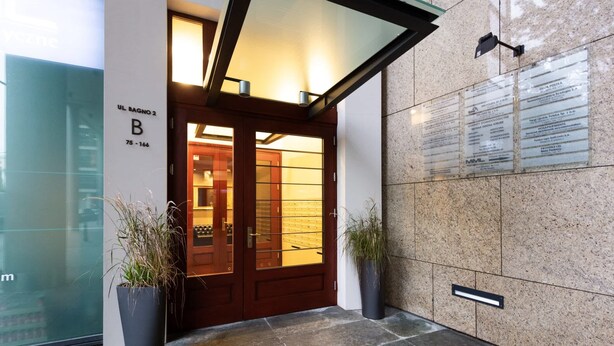 A hotel entrance with a wooden door, potted plants, and a stone wall with information plaques. - Modern Apartment in the Center | Balcony | Parking (Warszawa)