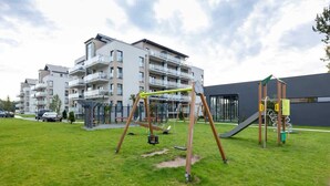 A playground with swings and a slide, surrounded by a grassy area and residential buildings.