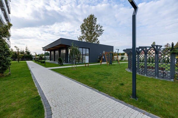 A modern building with a covered outdoor area, a paved walkway, and a playground.