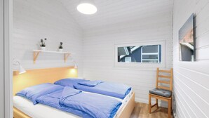 Een slaapkamer met twee bedden, een raam, een stoel en een plank met planten.