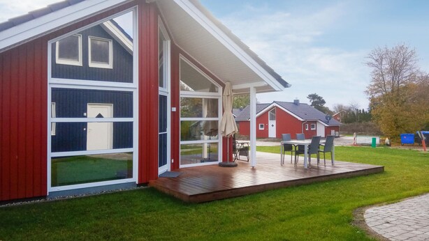 Een modern huis met een grote glazen deur, een houten terras en een rode gevel.