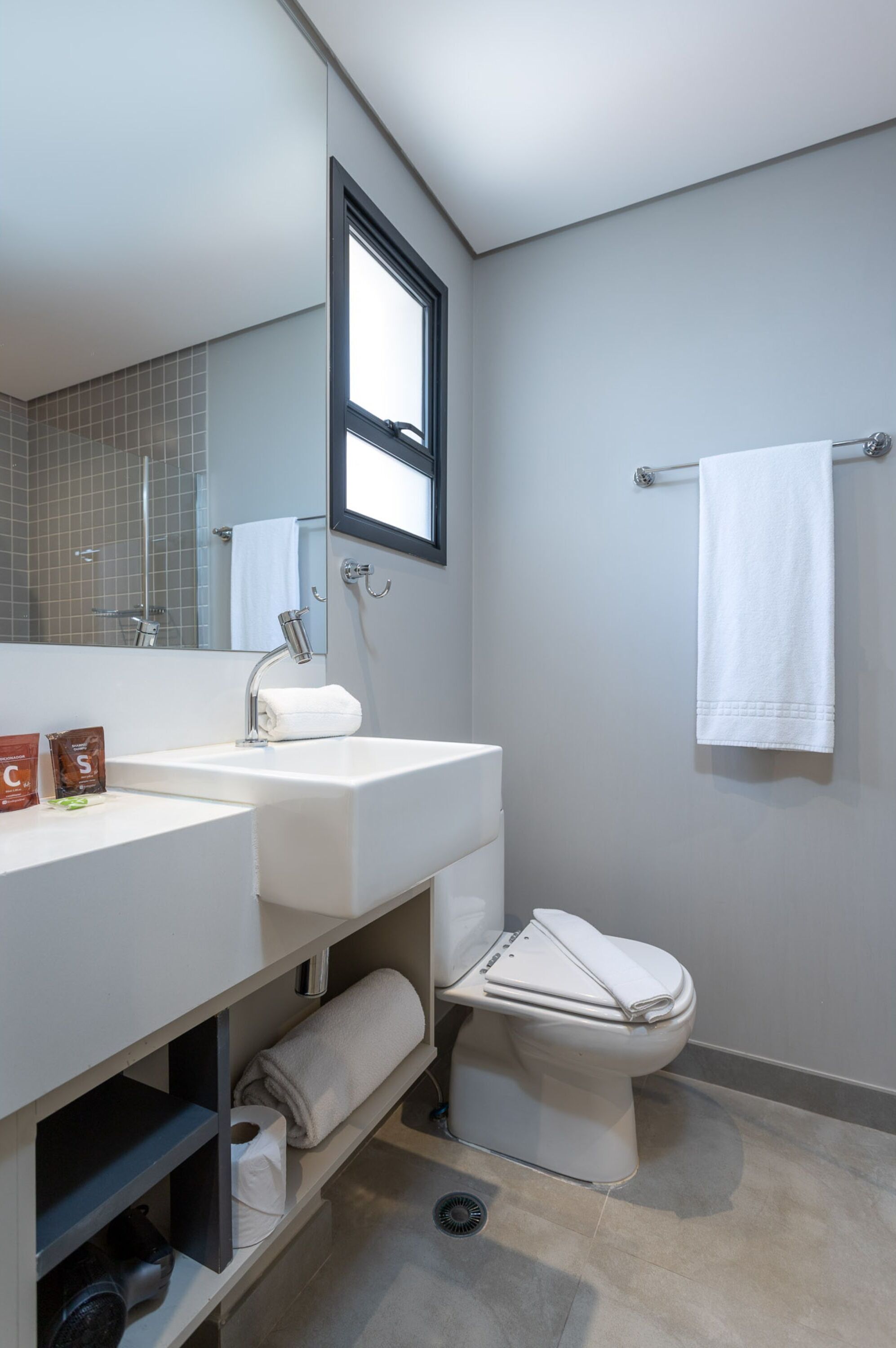 A modern bathroom with a white sink, mirror, and toilet. There are towels and toiletries on the sink.