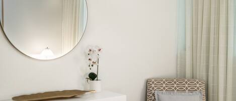 A bedroom with a bed, a bedside table, a mirror, and a window with curtains.