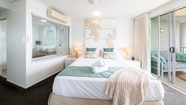 Ein modernes Hotelzimmer mit einem großen Bett, einer Duschkabine aus Glas und Blick auf den Außenbereich.