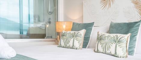 A hotel room with a bed, two pillows with palm tree designs, a bedside lamp, and a view of a balcony.