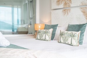 A hotel room with a bed, two pillows with palm tree designs, a bedside lamp, and a view of a balcony.