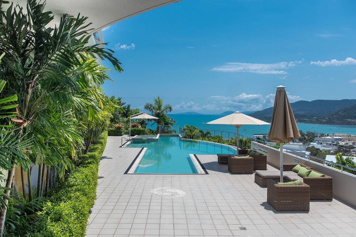 Zona de piscina en la azotea con vistas al mar, rodeada de vegetación y amueblada con asientos de exterior.