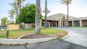 A hotel entrance with a guest registration sign, palm trees, and a modern building facade.