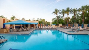 A swimming pool with lounge chairs and umbrellas, surrounded by palm trees and a building with a blue awning. - Club Wyndham Orange Tree Resort - 2 Bedroom (Scottsdale)