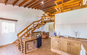 Cozy living space with a dining area, kitchen, and seating area, featuring a wooden staircase and a window.