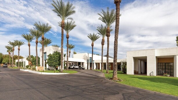 A modern hotel with a row of palm trees, a paved driveway, and a well-maintained lawn.